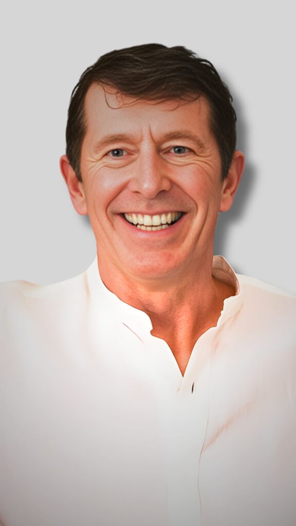A middle-aged man with short brown hair smiles warmly. He is wearing a white shirt with an open collar. The background is a plain, light gray color.